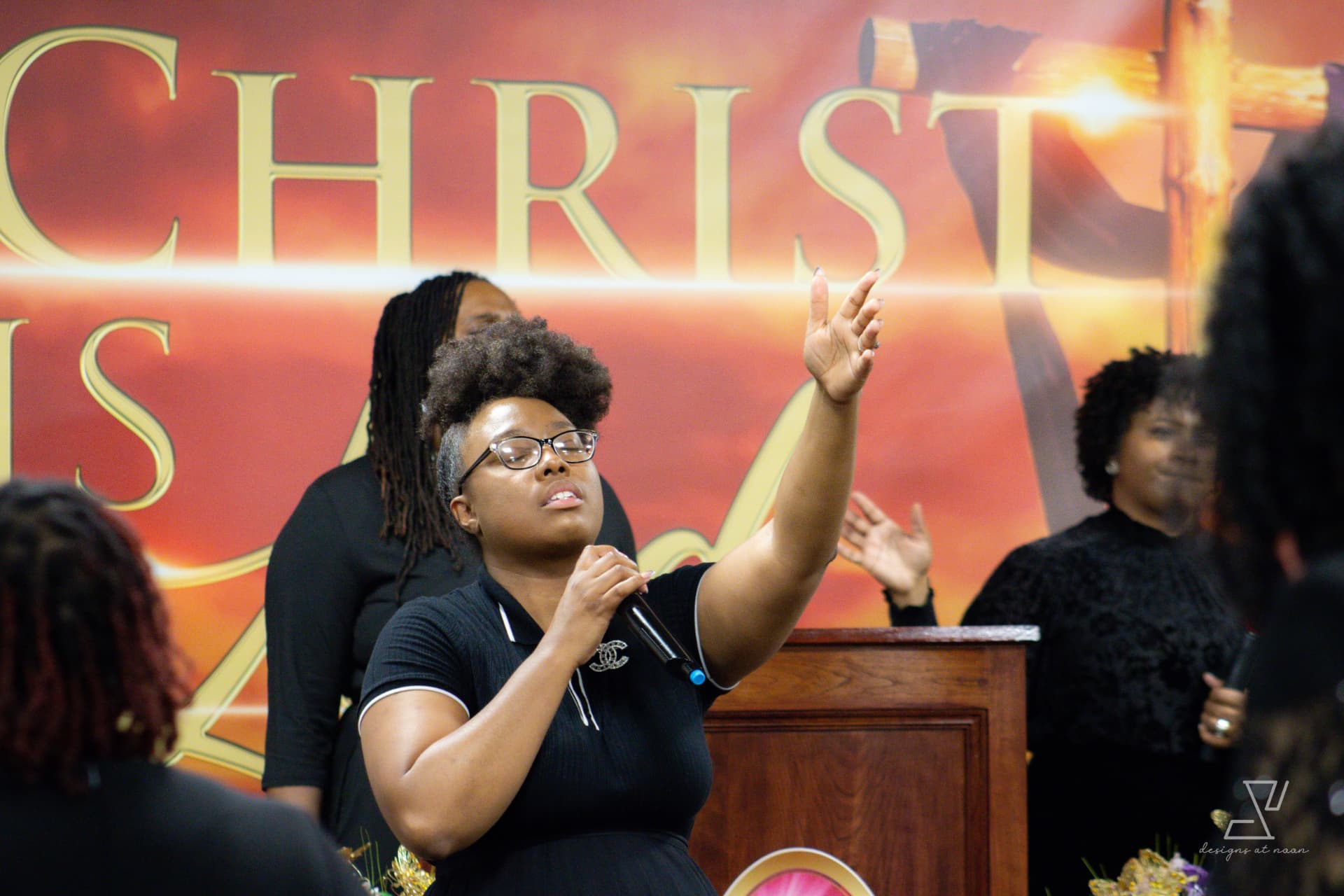 Young woman lifting her hand in worship while singing into a microphone