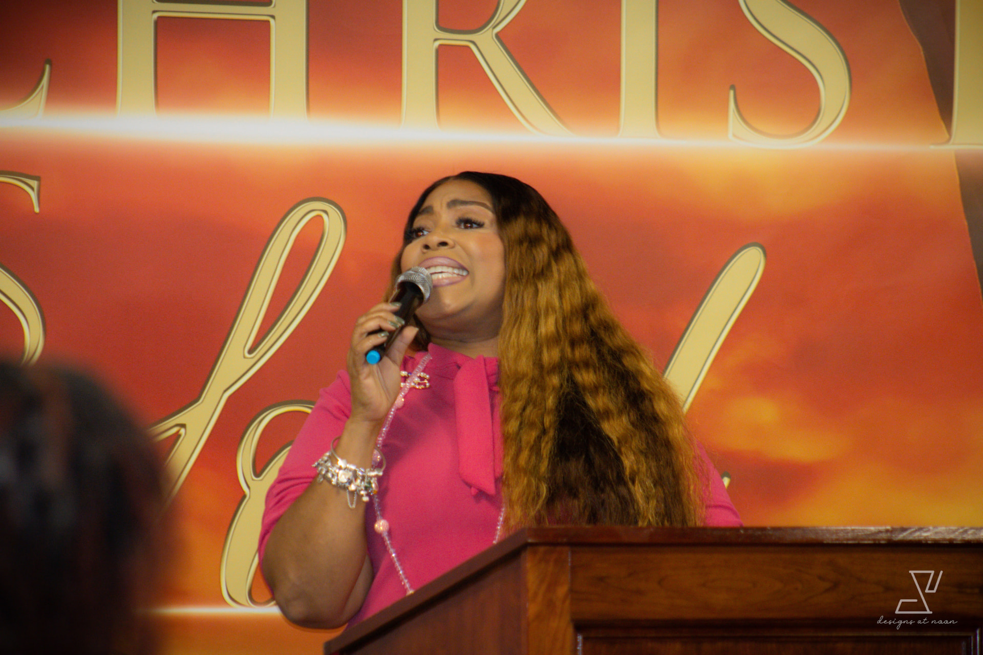 Woman in pink speaking into a microphone at the pulpit during worship