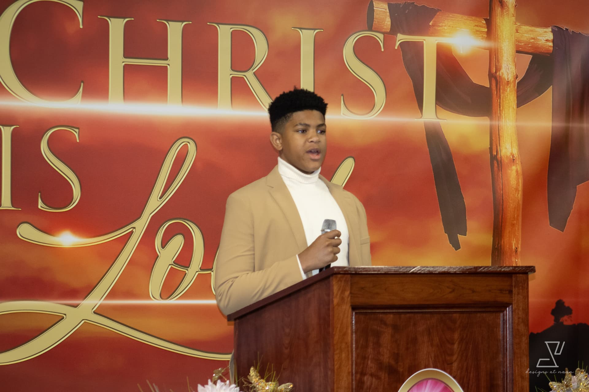 Teen boy in a tan blazer speaking at the pulpit during a church service